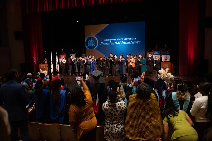 Audience applauding at the Governors State University Presidential Investiture ceremony, with dignitaries on stage.