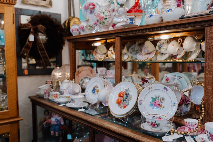 Antique store display featuring an array of vintage china teacups, teapots, and plates arranged in a wooden glass-fronted cabinet.