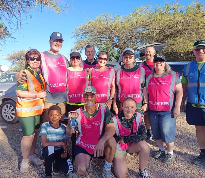 A group of parkrun volunteers smiling and taking picture on a sunny day.
