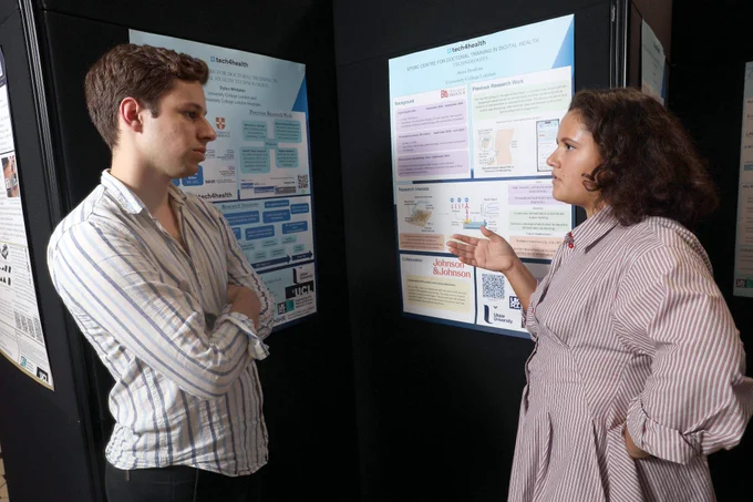 Two people talking with posters in the background.