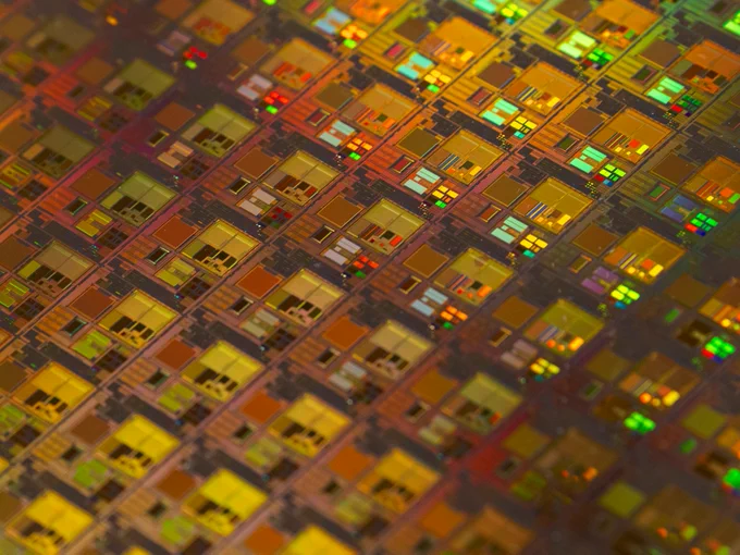 Close-up of a silicon wafer with colorful, reflective patterns of microchips, showcasing intricate circuit designs.