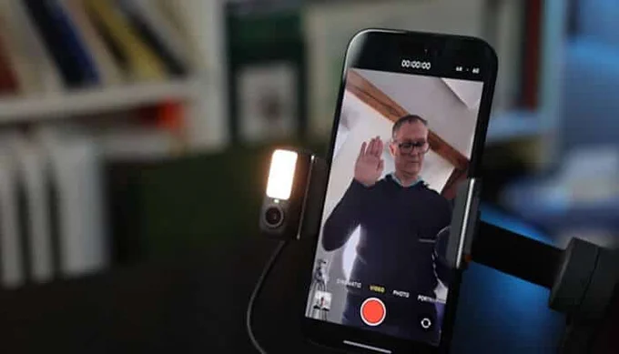 Person using DJI Mimo for PC app on a smartphone, recording a video with a camera setup and a tripod, featuring the interface of the app with a red recording button.
