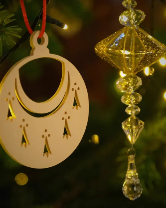 Close-up of a bauble in the shape of Trinity Hall's crest hanging beside a sparkling gold crystal decoration on a Christmas tree.