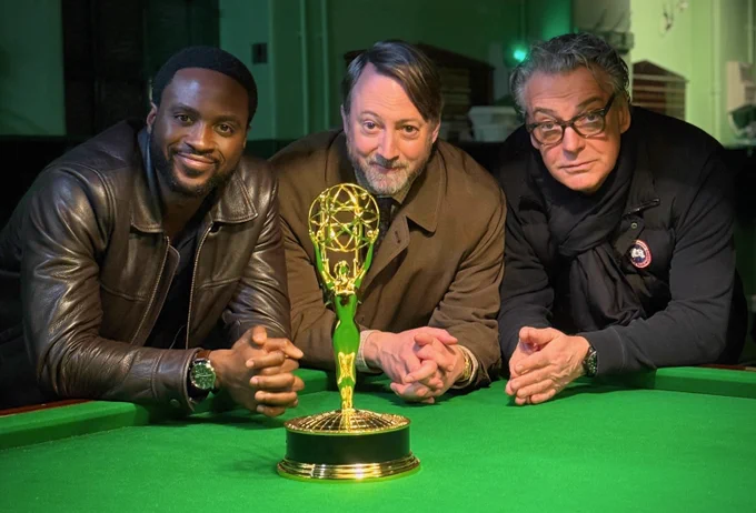Dipo Ola, David Mitchell and Kenton Allen lean against a snooker table, on which is standing an Emmy statuette