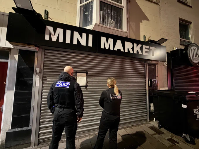 Trading Standards Officer and Police officer sticking closure notice a shop's shuttered doorway.
