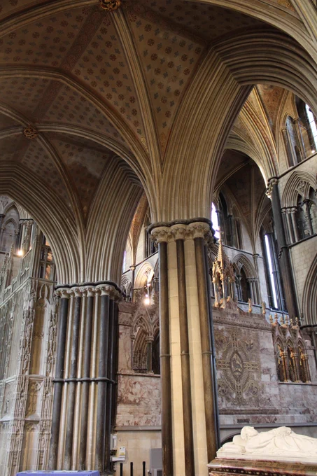 The pillars are of pale brown stone with black Purbeck Marble shafts. The ceiling of the south aisle of the Lady Chapel is painted with blue and red crosses. In the middle distance is the reredos and part of Prince Arthur's Chantry chapel. In the distance is the top level of the St. George Chapel.  Also in the foreground is the effigy of the Earl of Dudley a Victorian benefactor of the cathedral restoration project. 