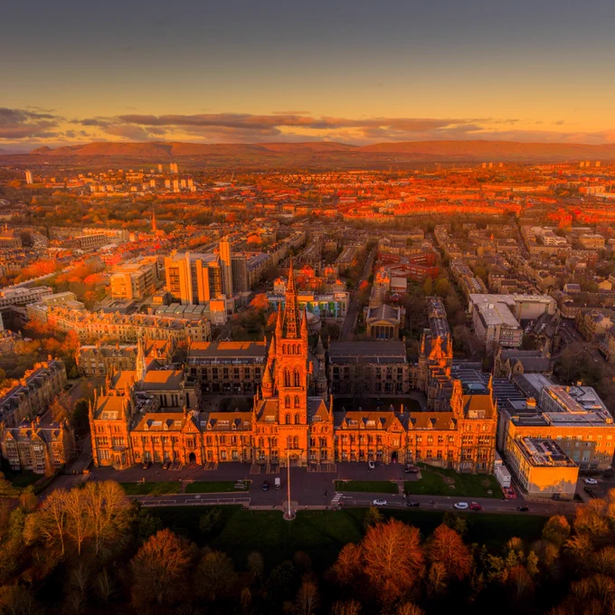 A drone image of the University of Glasgow Gilbert Scott building at sunset with the city in the background.