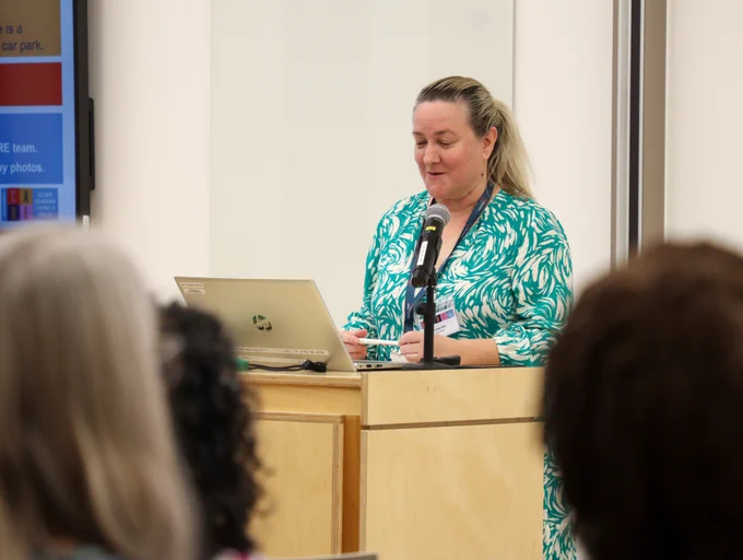 Person presenting at a podium with a laptop in front of an audience.