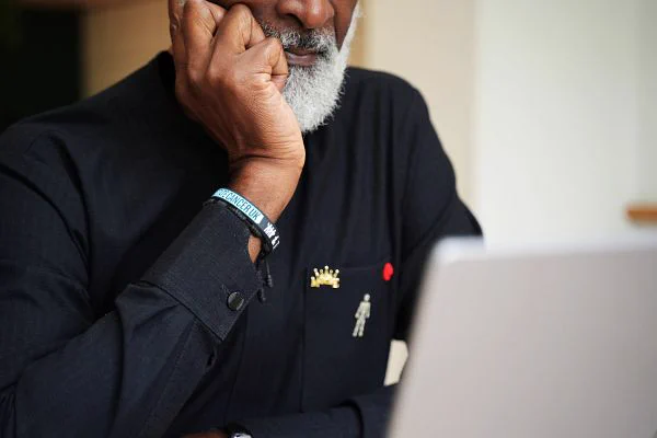The photo shows part of an older man with a gray beard, sitting at a laptop.