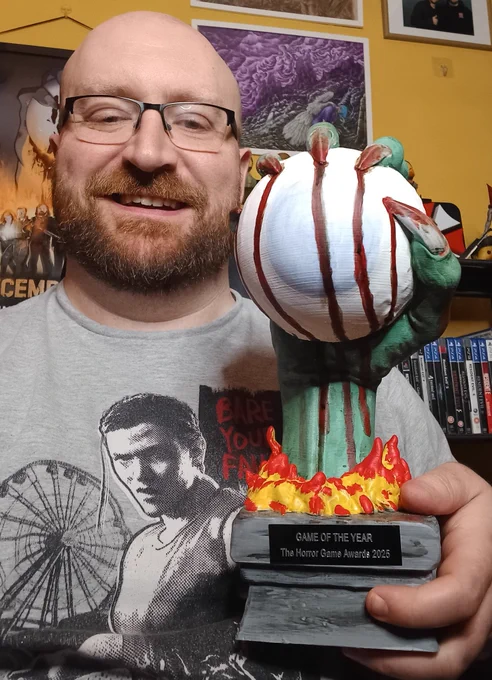 Me holding The Horror Game Awards 2025 Game of the Year trophy, a demonic claw gripping a large eyeball