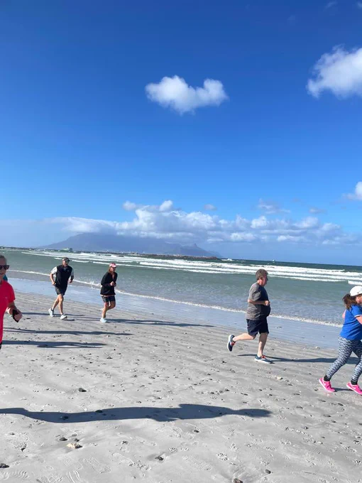 A group of parkrunners running on a sandy beach with a clear sky in the Big Bay parkrun.