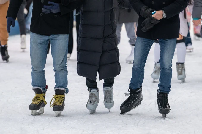 Three people ice skating on an outdoor rink, wearing winter clothes and holding hands for balance.