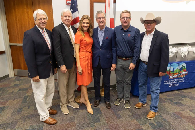 I pose for a photo with Florida leaders at the groundbreaking event. There are gift bags and an American flag behind us.