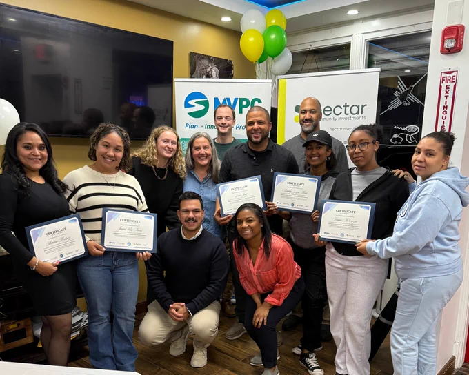 A group shot of twelve smiling people including a range of ethnicities and genders. Five people are holding certificates from the program. 