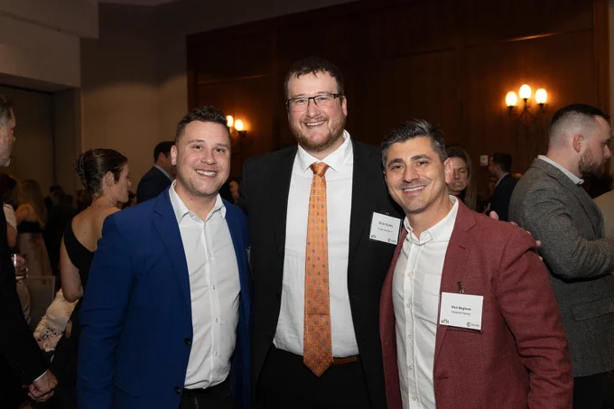 Three men in formal attire stand together smiling at the camera