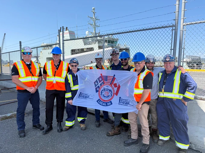Local 58 Flag at Davie Shipyard (L–R): Jamie Andre (International Representative Eastern Canada), Michael MacDonald (MacKinnon & Olding Vice President), Robert Boudreau (Member of Local 58), Pierre Gollain (Business Manager of Local 58), Sebastien Villeneuve (Member of Local 58), Stephane Chamberland (Member of Local 58), Richard Chartrand (Business Agent of Local 58), Charlie Prefontaine-Noreau (Member of Local 58), & Jean-Paul Cote (Member of Local 58), background ft. one of the first ships to undergo a major refit