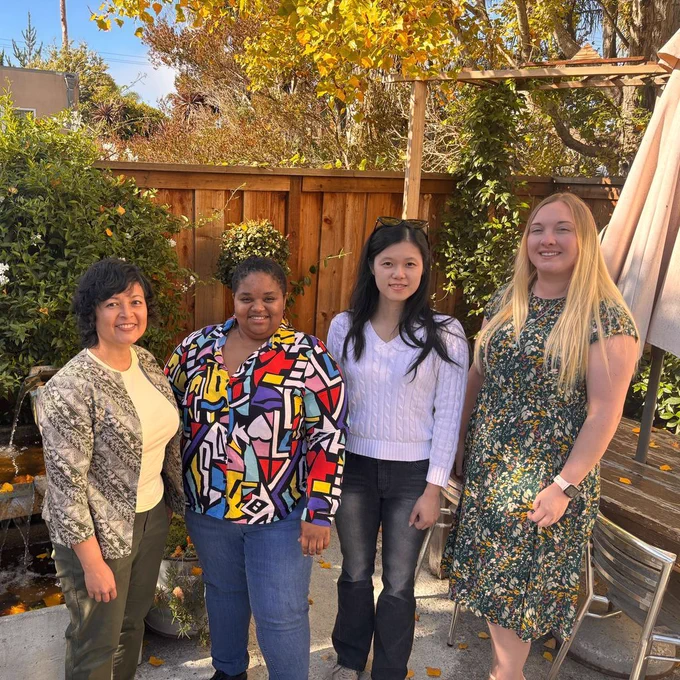Four people with varying clothing and hair colors gathered in an outdoor space on a sunny day