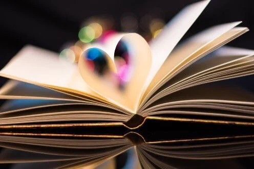 an open book with a heart shape in the middle, there are lights twinkling in the background. 