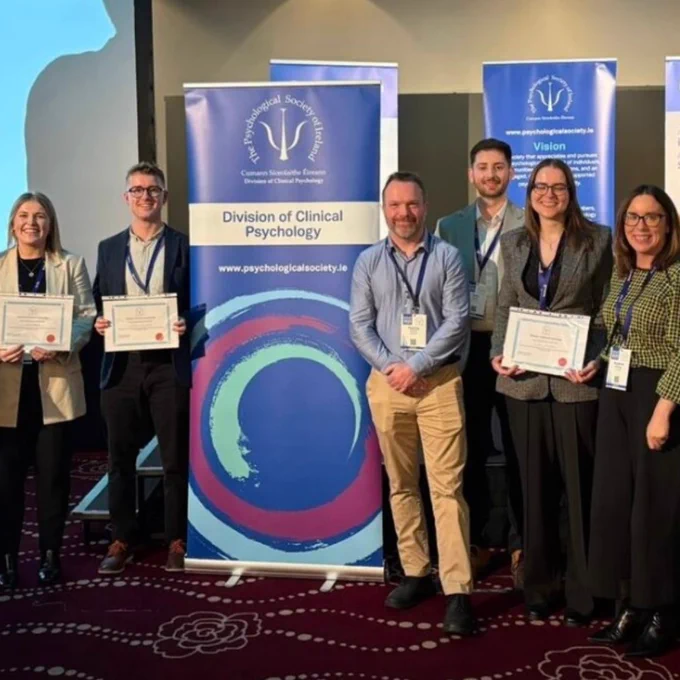 Group of professionals standing in front of banners for the Psychological Society of Ireland, some holding certificates at a conference event.