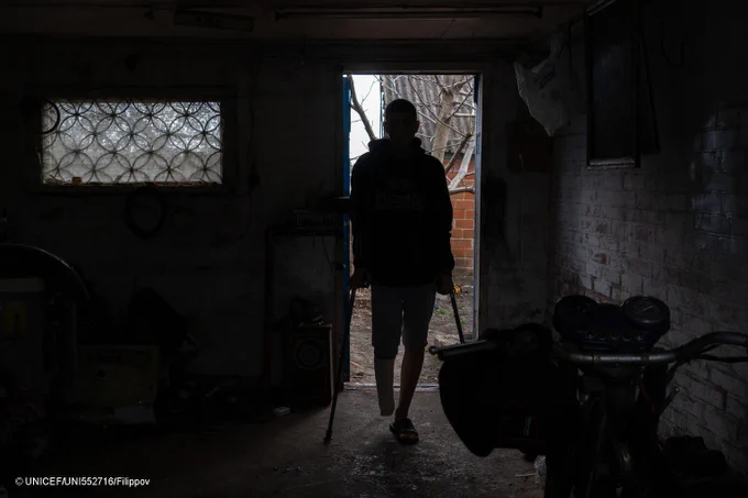 Silhouette of a boy with crutches who stands in the doorway of his home