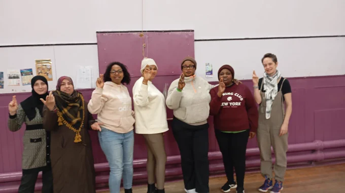 A group of Black and Brown women crossing their fingers in front of a horizontally painted pink and white wall