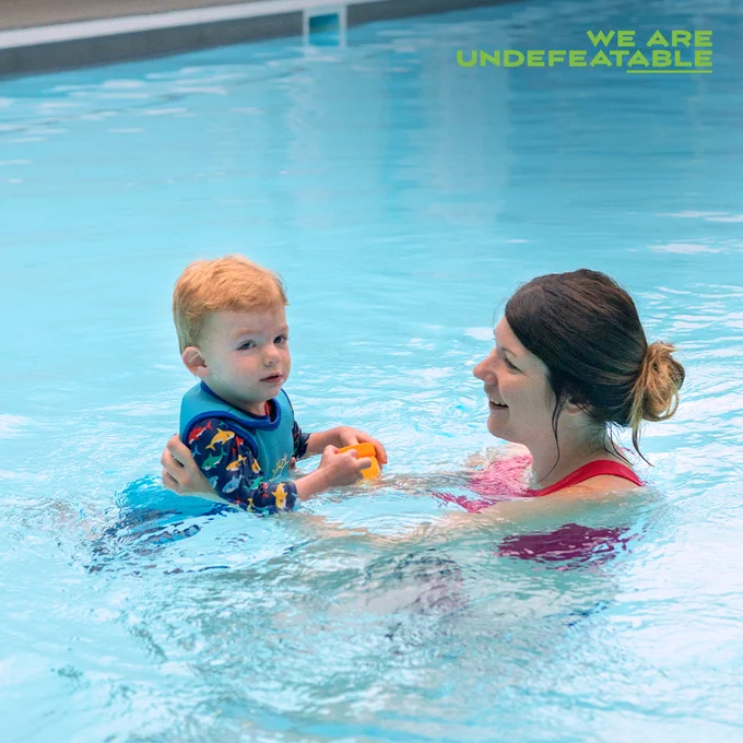 A boy and a woman swimming in a pool, both looking at each other and smiling, with the text "We Are Undefeatable" at the top.