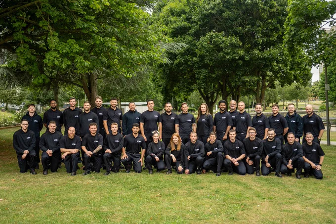 A group of 33 UK Power Networks experienced apprentices pose together for a group photo. They are standing in a park outside.