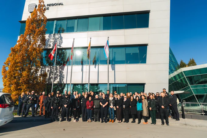 Large group of individuals standing in front of building with flags raised behind them