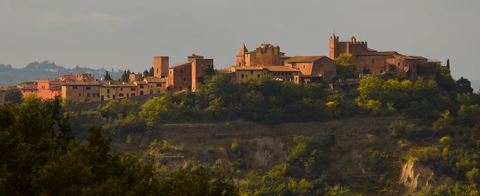 Scenic red stone buildings sit atop a mountain in Tuscany.