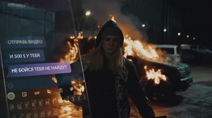A still from an SBU video for a publicity campaign warning young people not to allow themselves to be recruited as saboteurs. The fictionalised image shows a hooded teenage girl walking from a van she has just set fire to at night. In the left of the screen is an untranslated image of the girl's phone messaging exchanges with the person who has ordered her to carry out the attack.
