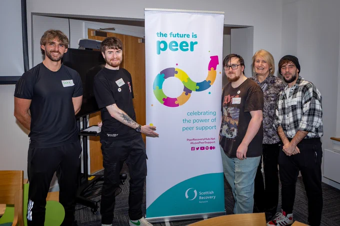 5 event participants standing next to a roller banner which reads "the future is peer"