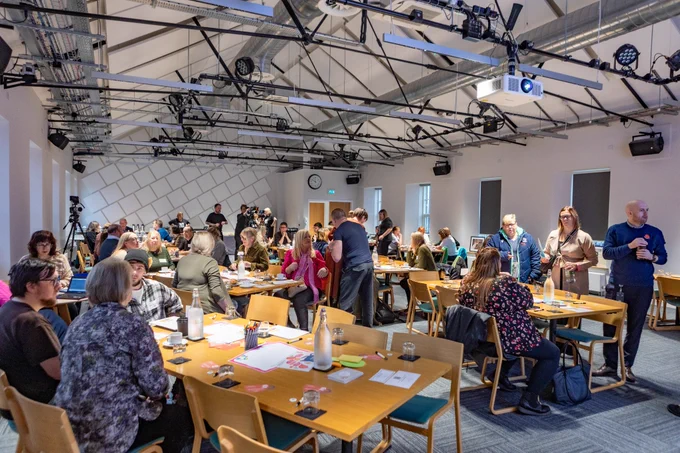 A room full of event participants sitting at tables or standing.