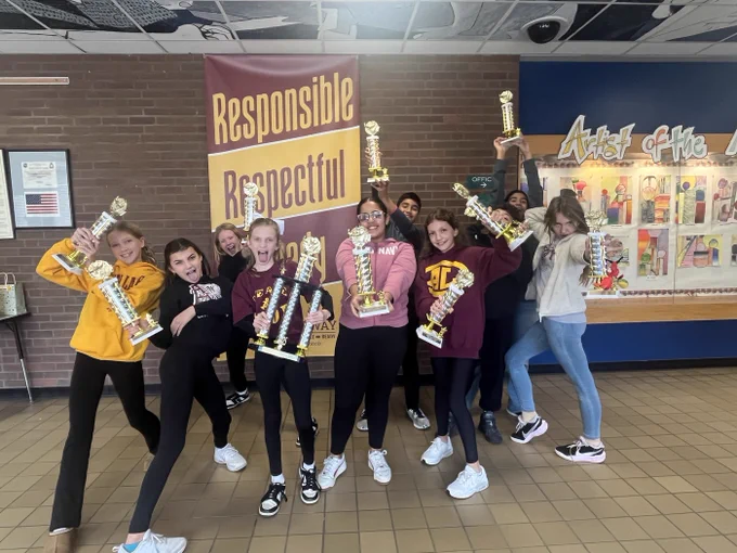 Troy students hold up their first place trophies inside the school building.