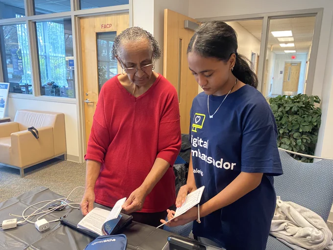 A young woman helps an older woman with a tech device 