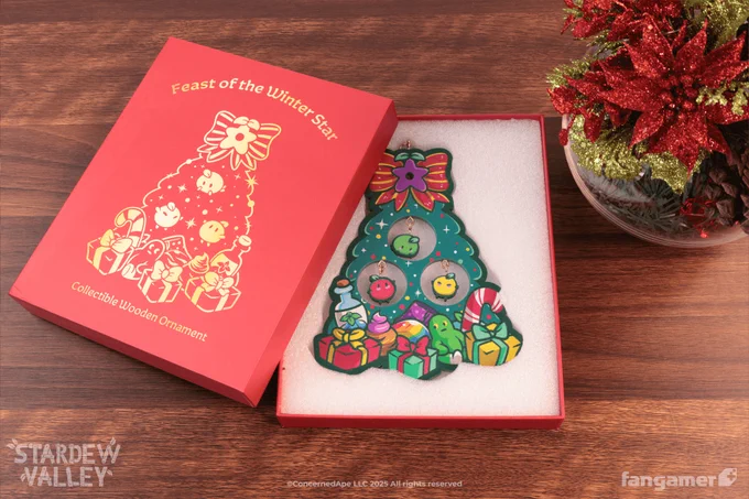 A photo of the Feast of the Winter Star ornament in its red keepsake box. It's a wooden ornament of a decorated tree with presents at the bottom and three Junimos hanging like ornaments in round cutouts. 