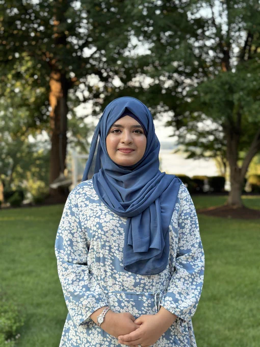 Aneeza Khan poses outside, wearing blue business casual clothing.