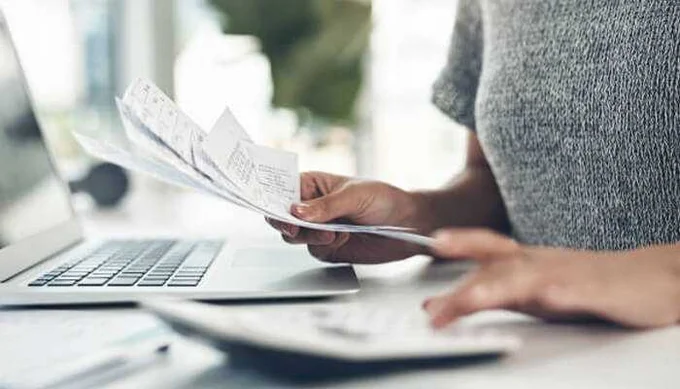 A person reviewing bills and invoices on a laptop while calculating costs — illustrating careful telecom expense management and budgeting.
