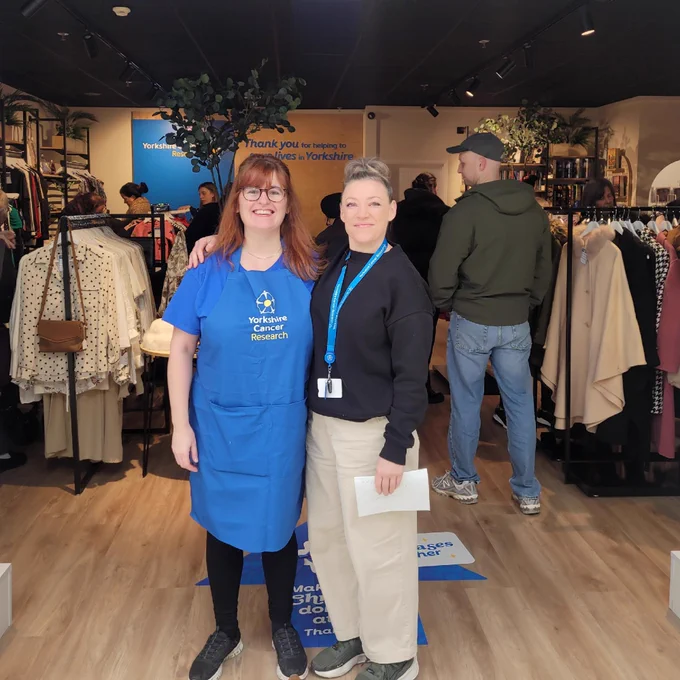 Members of the Yorkshire Cancer Research team standing at the entrance of the charity's new shop in Sheffield Crystal Peaks shopping centre. One is wearing a branded apron.