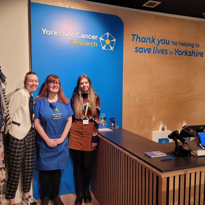 The Yorkshire Cancer Research shop team stand near the till area of the Yorkshire Cancer Research shop in Sheffield. The words "Thank you for helping to save lives in Yorkshire" is visible on the wall.