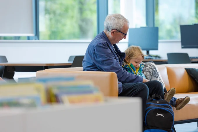 older person with glasses sitting with a young person in a library setting