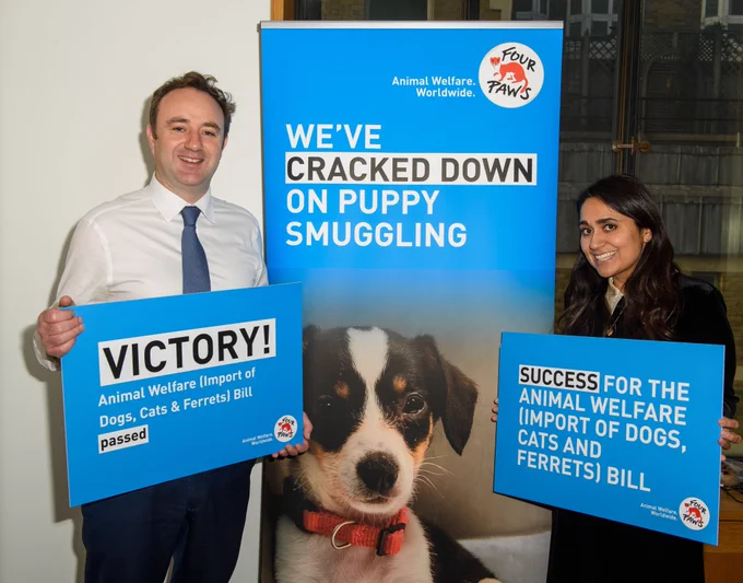 Dr. Danny Chambers MP and FOUR PAWS UK Country Director Sonul Badiani-Hamment celebrate passing of the Animal Welfare Bill. Sign reads - "We've cracked down on puppy smuggling". "Success for the Animal Welfare Bill".