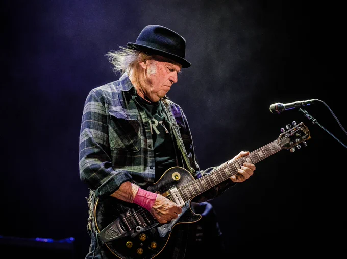 Neil Young plays guitar on stage.