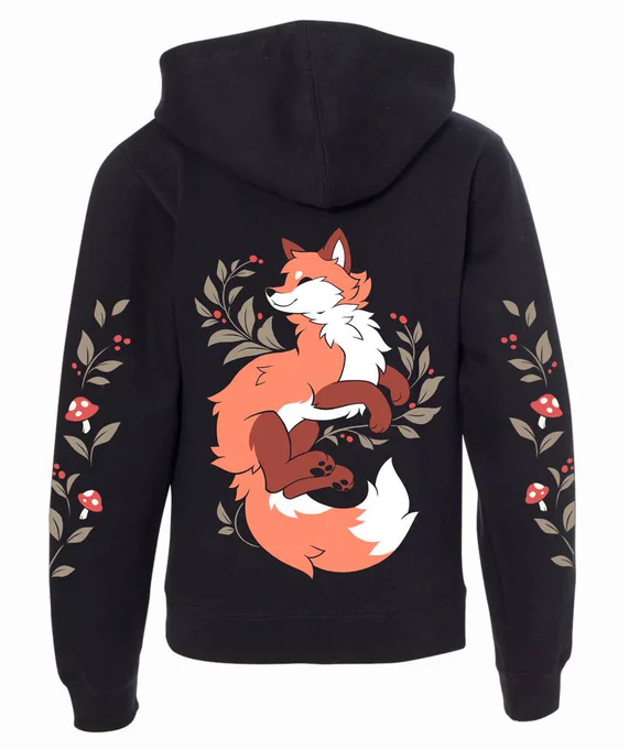 A zipper hoodie featuring fox artwork on the back. The fox is smiling with its eyes closed and its paws in the air. Its fluffy tail is curled upward. There are small plants with berries surrounding it. The sleeves are decorated with mushrooms and leaves.