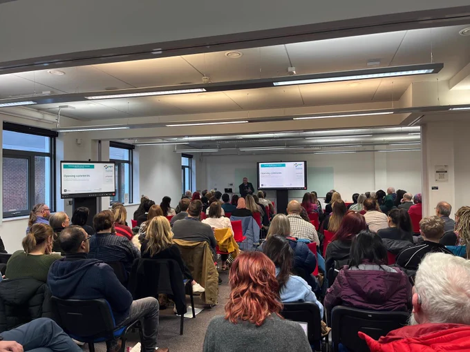 Around 100 conference delegates are facing a person delivering a presentation