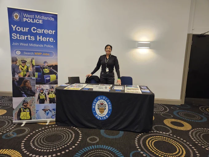 PC Begum standing behind a table at the CTP event with a West Midlands Police banner.