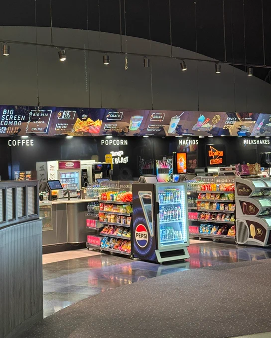 Image of a cinema concession stand displaying various snack options including popcorn, nachos, and milkshakes. 