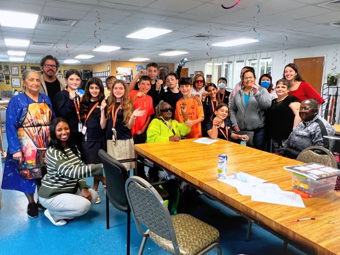 A group photo of 24 people, students, seniors, and staff, smiling for the camera at Miami Lighthouse.