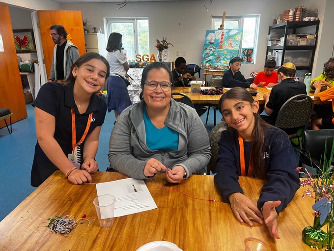 A group photo of two students and one SGA participant at Miami Lighthouse during a student volunteer visit, smiling for the camera while working on an art project.