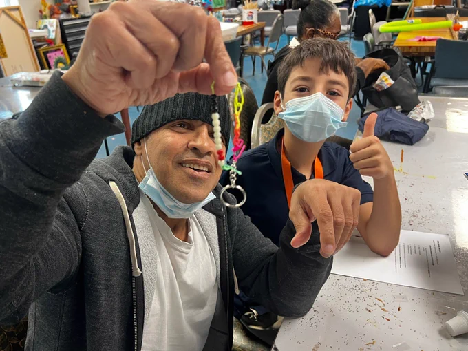 An SGA participant and JLA student pose for the camera, while holding up their white cane keychain creations that they made together.
