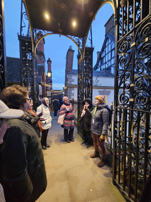 Female tour guide standing alongside Eastgate Clock in Chester. Visitors listing. Nearly dusk on an autumnal day. 